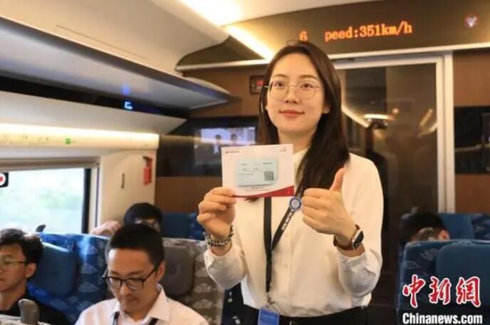 列車の中で乗車券を手にポーズをとる乗客。後方上部は列車の走行速度の表示。（撮影?李志全）