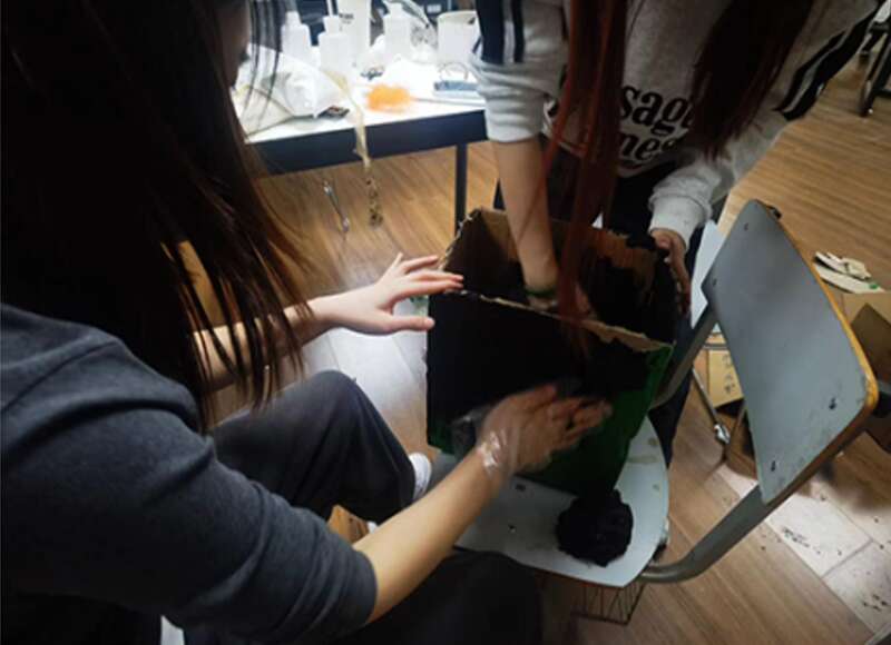 コーヒーかすを段ボールに塗り付ける學(xué)生。