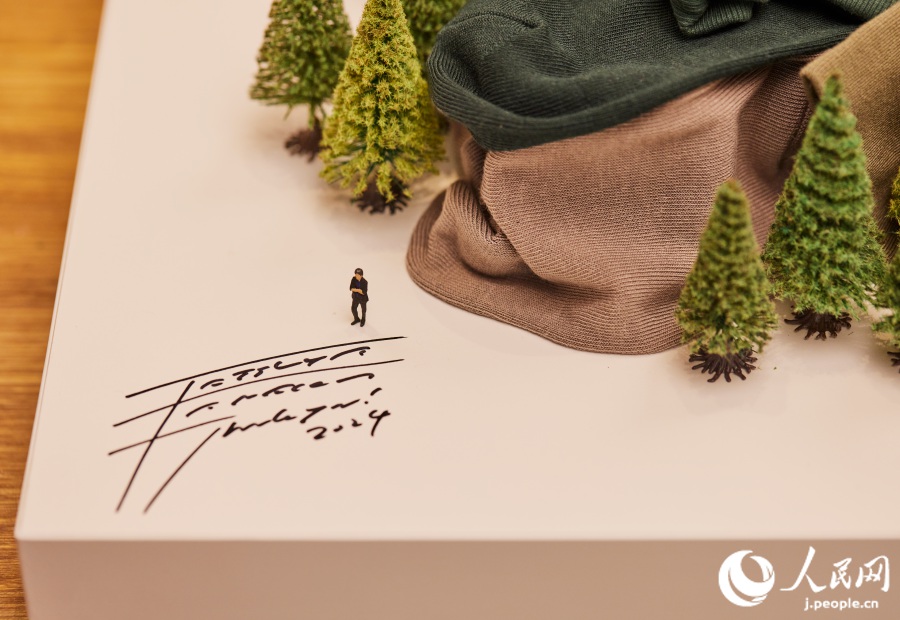 作品「想像の長城」の左端に書かれた田中達也氏のサインと田中氏自身のミニチュア人形（寫真提供?MUJI HOTEL 北京）。