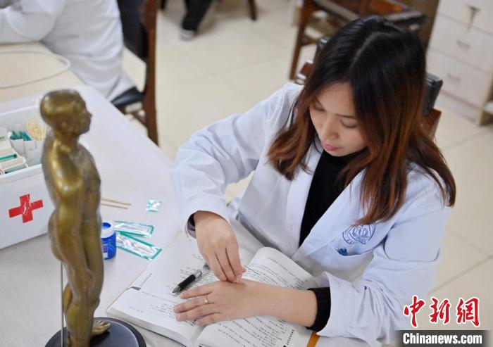 休憩時間に、中醫(yī)學(xué)の本を見ながら、銅人に鍼を刺入する経穴の位置を確認(rèn)する林玉花さん（撮影?張瑤）。