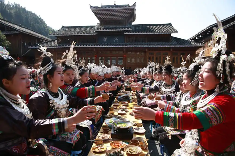 長いテーブルに料理を並べた宴會「長卓宴」で乾杯する侗族の女性たち（撮影?楊代富）。