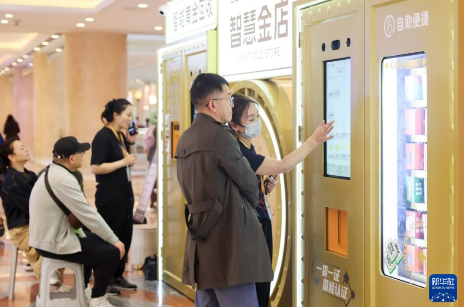 上海市普陀區(qū)の商業(yè)施設(shè)にある「スマート金買取?販売ショップ」で、セルフサービスの金購入裝置の金製品について利用客に説明する店員（5月5日撮影?王翔）。