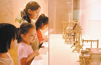 カザフスタンの小學(xué)生が「絹とシルクロード、中國(guó)からカザフスタンへ」展で、織機(jī)と糸繰り機(jī)の模型を眺める様子（撮影?陳尚文）。