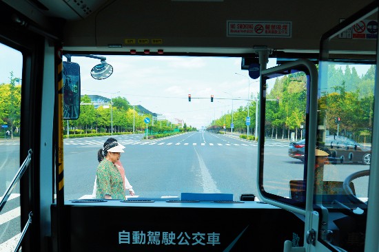 赤信號(hào)で自動(dòng)で停車したB19自動(dòng)運(yùn)転バスの前を歩く歩行者。