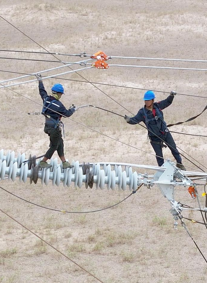 7月12日、陳林さん（右）と同僚が新疆維吾爾（ウイグル）自治區(qū)和田（ホータン）地區(qū)民豊県の工事現(xiàn)場(chǎng)で、送電線(xiàn)の架線(xiàn)作業(yè)を進(jìn)める様子。（ドローンによる撮影）