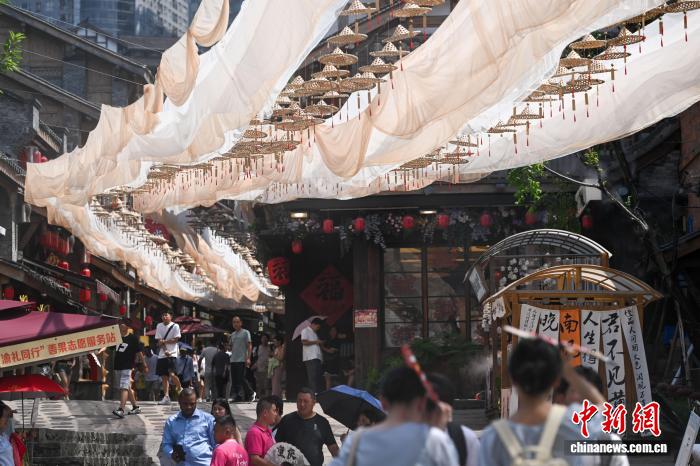 重慶市の十八梯伝統(tǒng)風貌區(qū)で、かぶり笠と布で張られた天幕の下を歩く観光客。（7月29日撮影?何蓬磊）