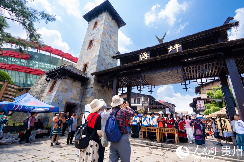 彝族の風(fēng)習(xí)である客を歓迎する「攔門(mén)酒（歓迎の酒）」を體験する場(chǎng)所で寫(xiě)真を撮影する観光客たち（撮影?涂敏）。