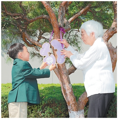 3月25日、「平和音楽の木」にQRコードを取り付ける大門高子氏（右）と南京紫金草童聲合唱団の団員。このQRコードから、「平和の花 紫金草」を聴くことができる。寫真提供：中國侵略日本軍南京大虐殺遭難同胞紀念館。