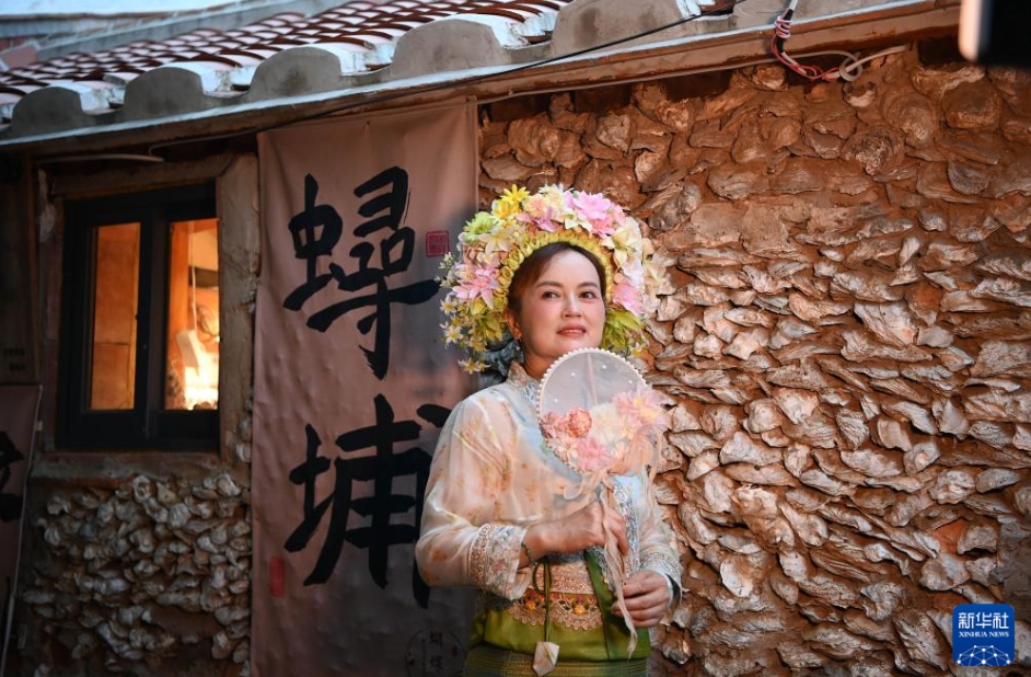 蟳埔村の牡蠣の殻と海の砂を使って作られた伝統(tǒng)家屋「蚵殼厝」の前で記念寫真を撮影する「簪花圍」で髪を飾った女性。（8月18日撮影?肖瀟）