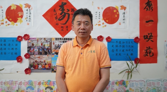 介護施設「一笑苑」內(nèi)の壁に飾られた寫真や書畫の作品の前に立つ「一笑苑」代表取締役の佐々木弘志さん（撮影?許可）。