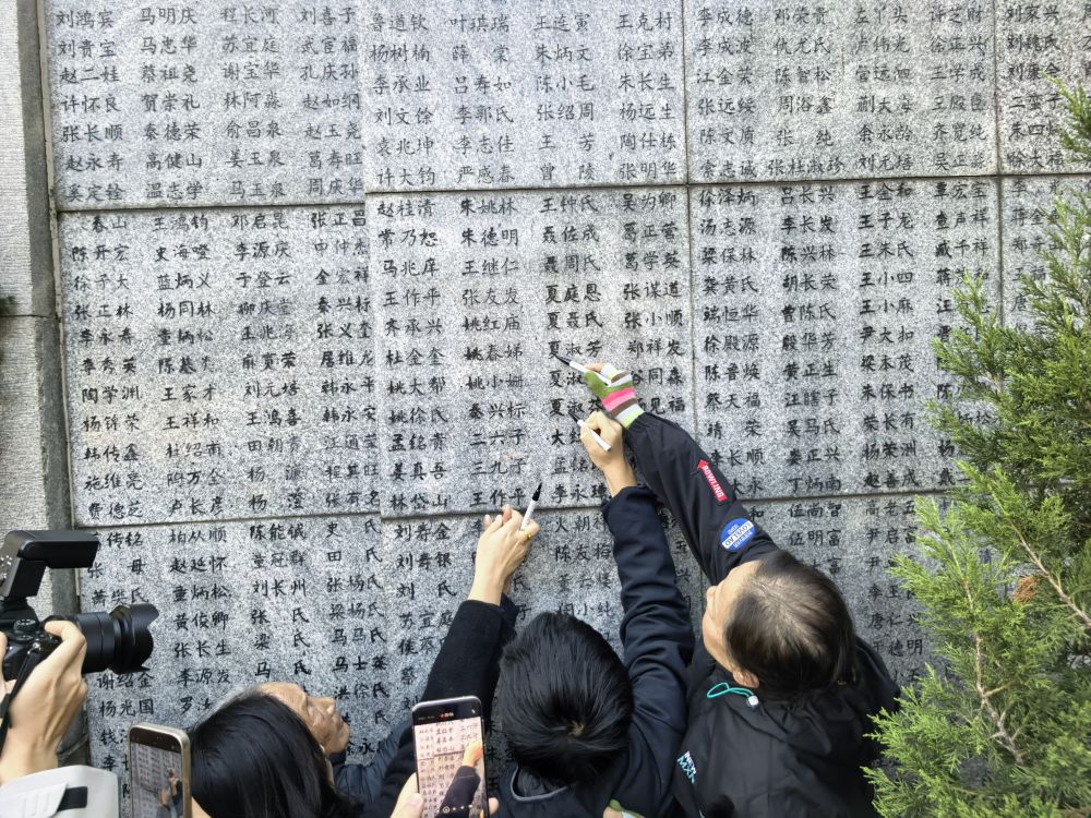 「嘆きの壁」に刻まれた親族の名前を指す南京大虐殺の生存者?夏淑琴さん。その橫で名前を塗りなおす娘とひ孫（撮影?邱氷清）。